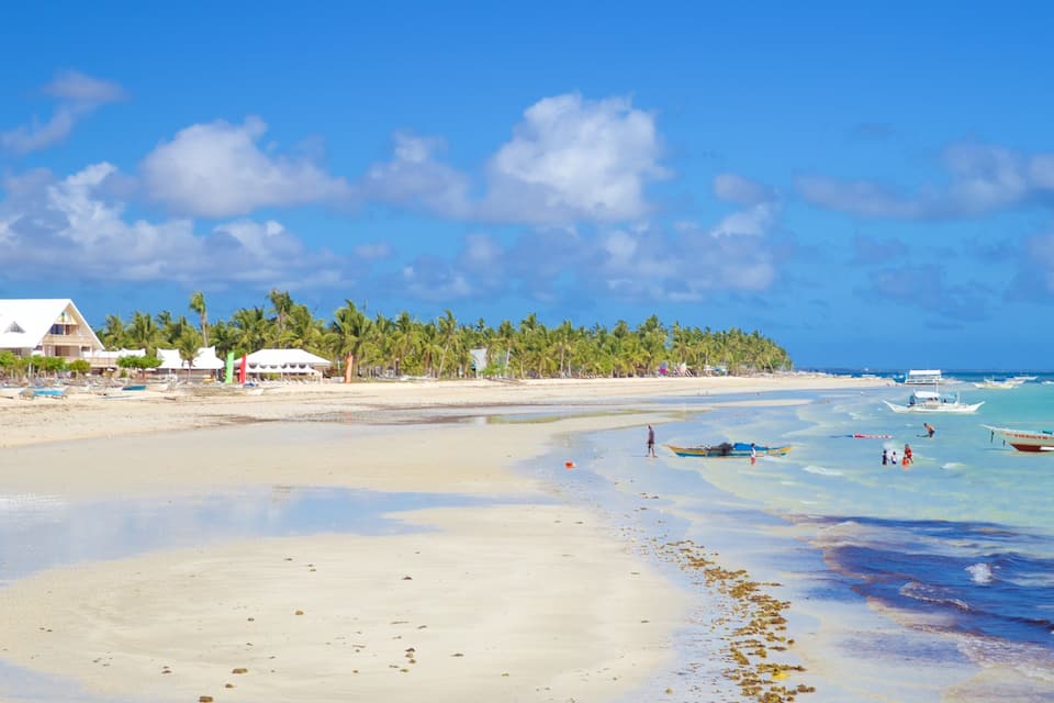 Ein Strand mit klarem türkisblauem Wasser, einem Sandstrand und einer Reihe von Palmen.
