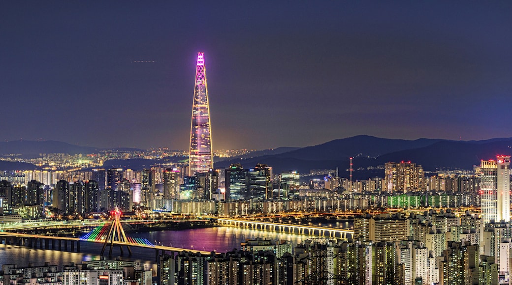 Gwangjin-gu, Seoul, South Korea - March 10, 2024: Night view of apartments with Olympic Bridge and Jamsil Railroad Bridge on Han River against Lotte World Tower