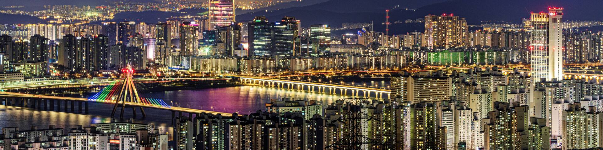 Gwangjin-gu, Seoul, South Korea - March 10, 2024: Night view of apartments with Olympic Bridge and Jamsil Railroad Bridge on Han River against Lotte World Tower