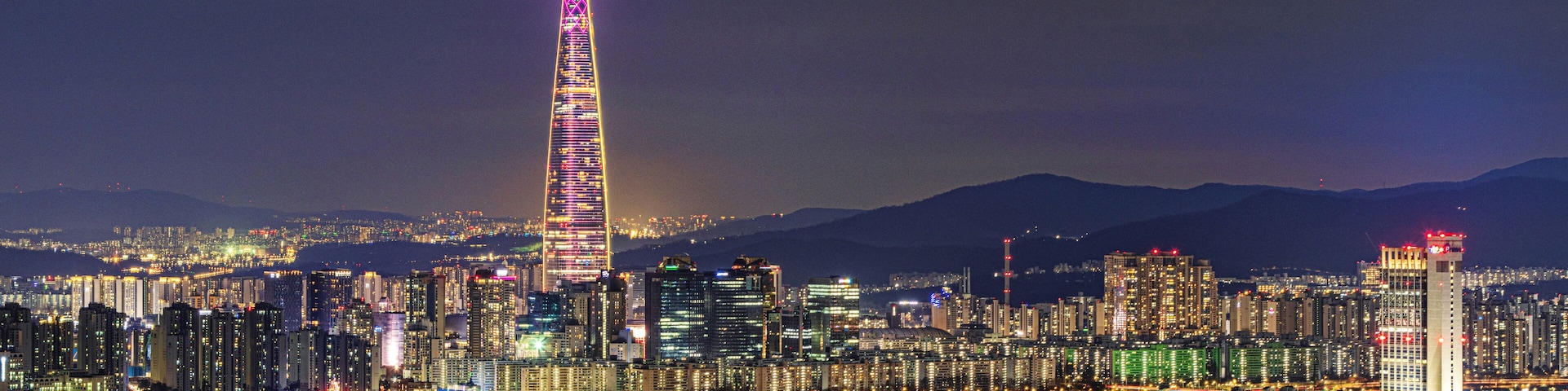 Gwangjin-gu, Seoul, South Korea - March 10, 2024: Night view of apartments with Olympic Bridge and Jamsil Railroad Bridge on Han River against Lotte World Tower