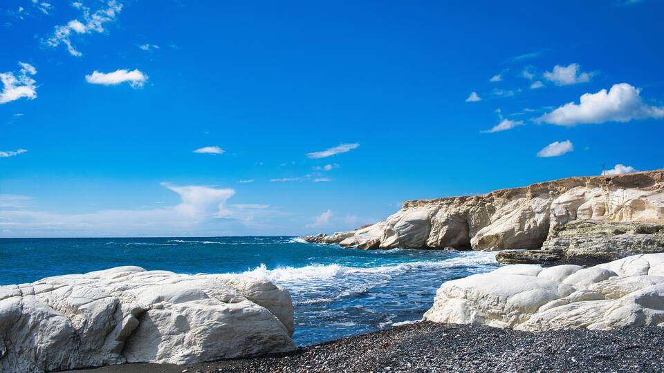 A rocky coastline with white cliffs and a pebbly beach under a clear blue sky.