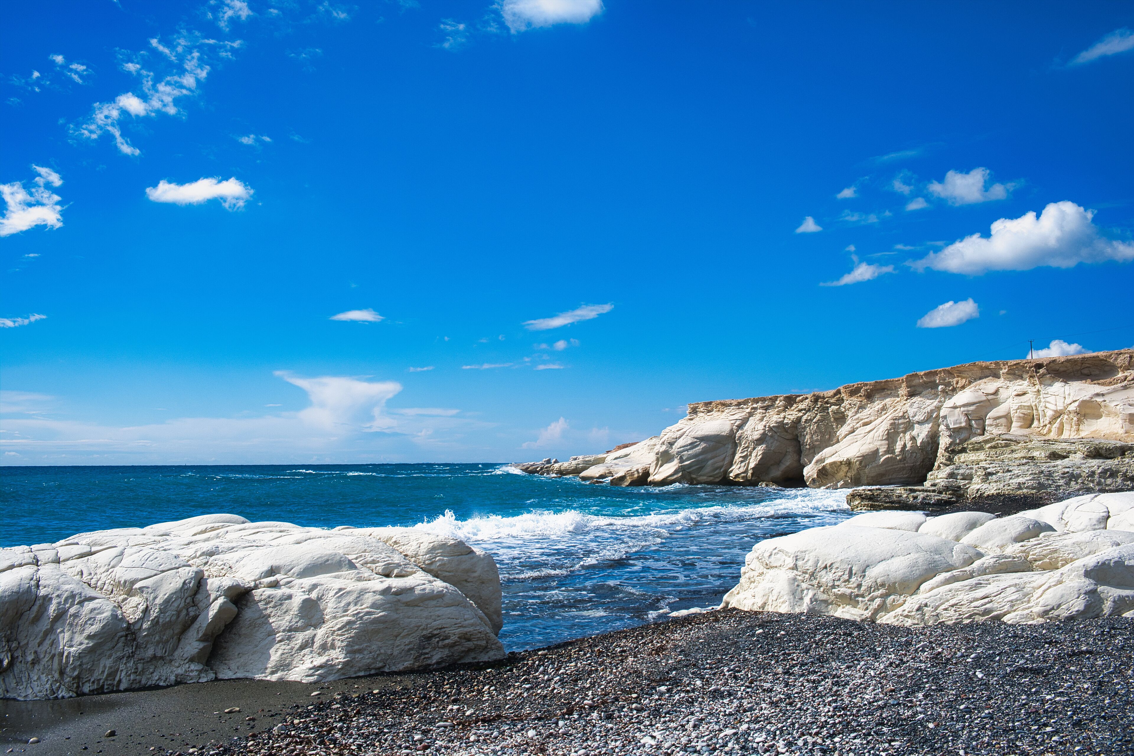 A rocky coastline with white cliffs and a pebbly beach under a clear blue sky.