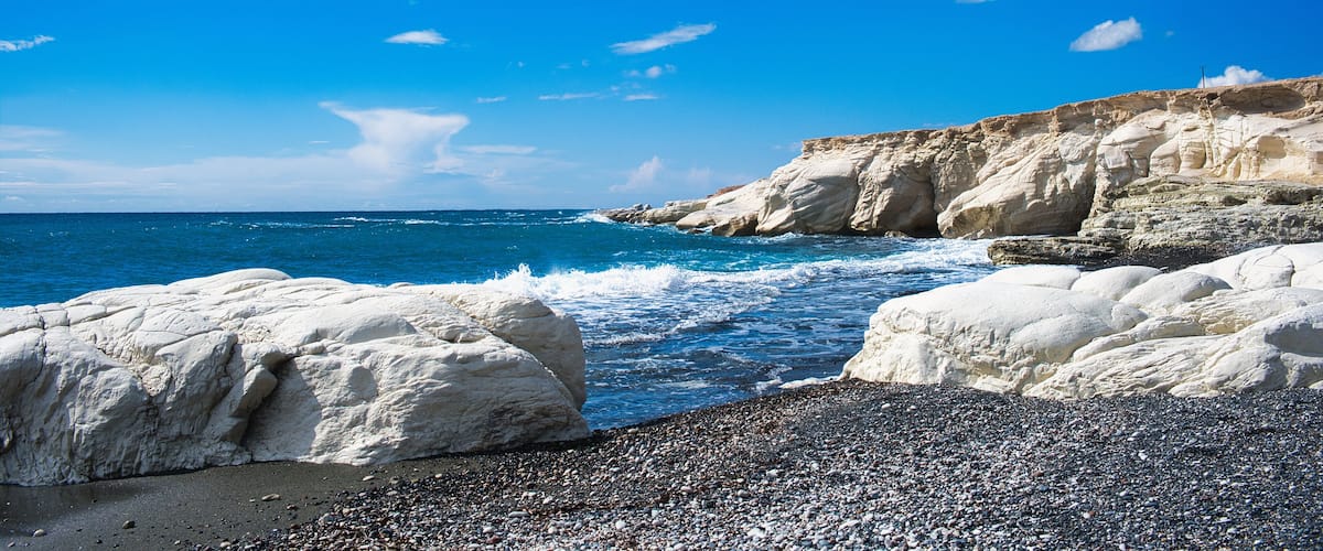 A rocky coastline with white cliffs and a pebbly beach under a clear blue sky.
