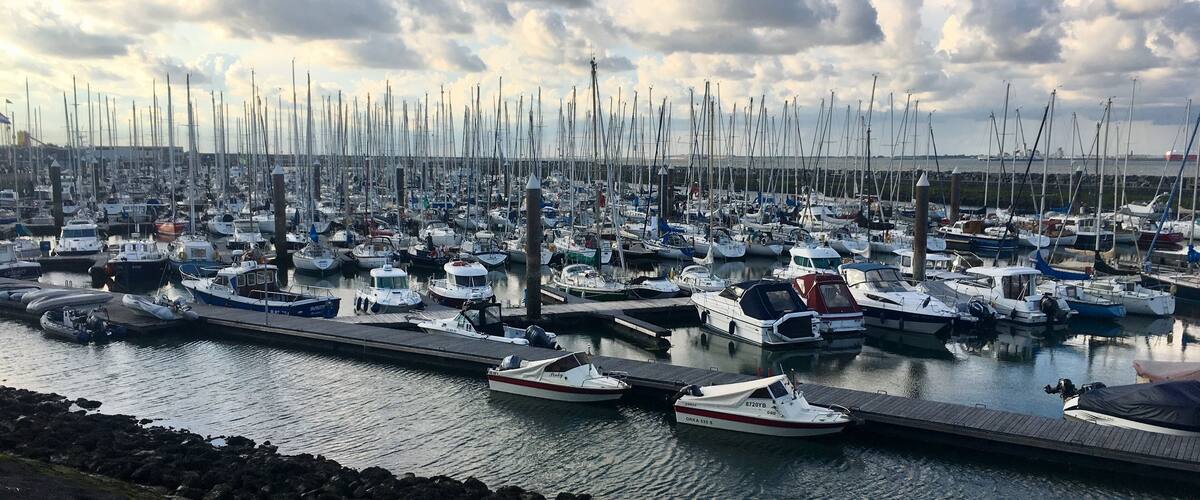 A marina filled with numerous sailboats docked at wooden piers under a partly cloudy sky.