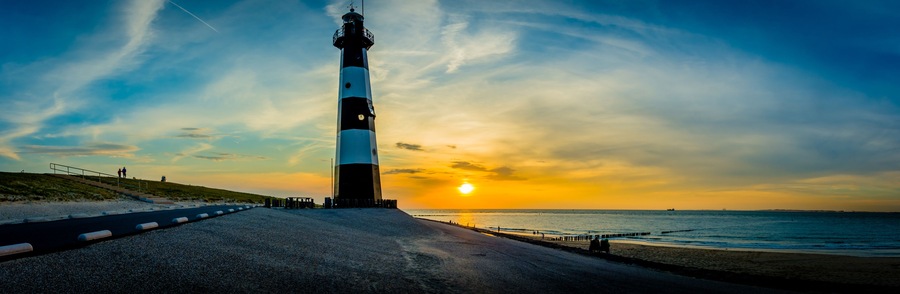 A lighthouse by the sea at sunset with a clear sky.