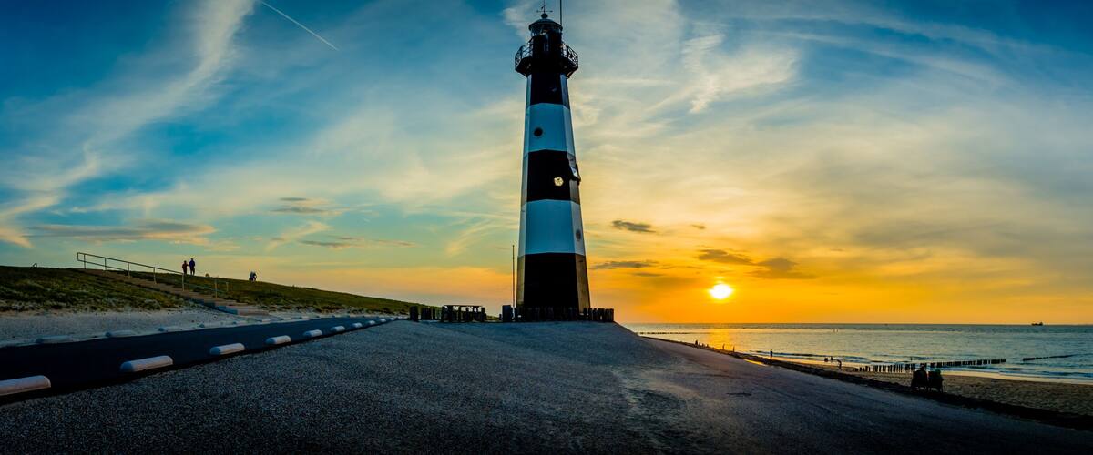 A lighthouse by the sea at sunset with a clear sky.