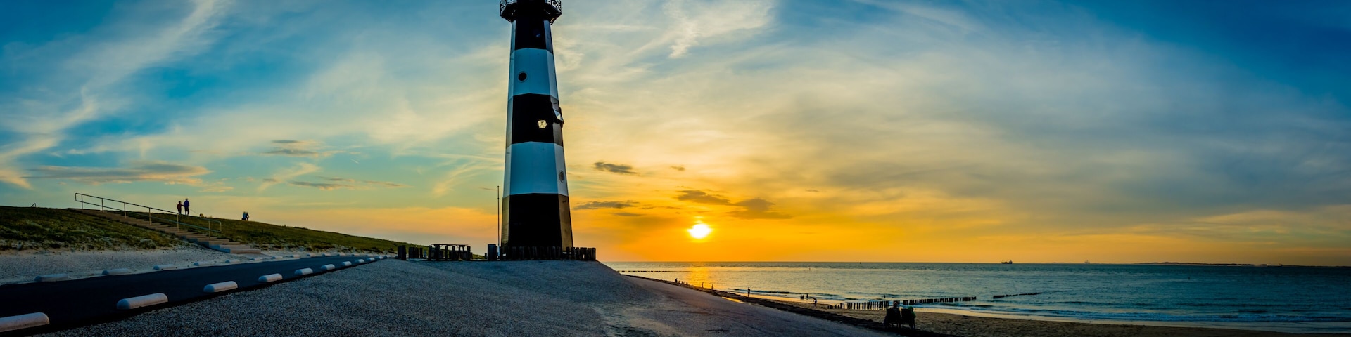 A lighthouse by the sea at sunset with a clear sky.