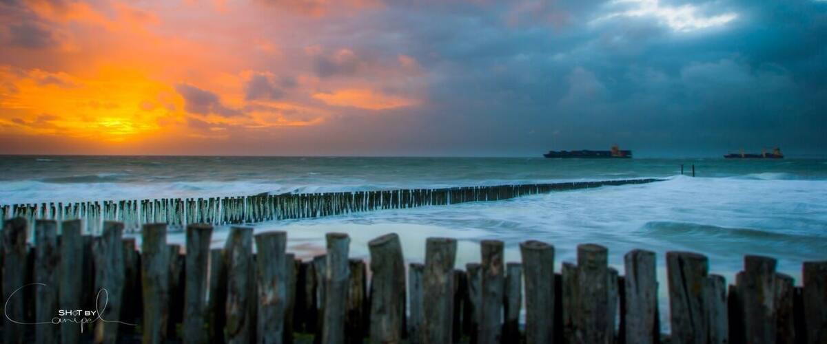 A sunset over the ocean with a wooden breakwater in the foreground.