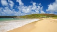 Une plage à l’eau turquoise et limpide, un rivage sablonneux et, en arrière-plan, une colline couverte de végétation.