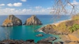 A coastal landscape with two prominent rock formations surrounded by turquoise waters.