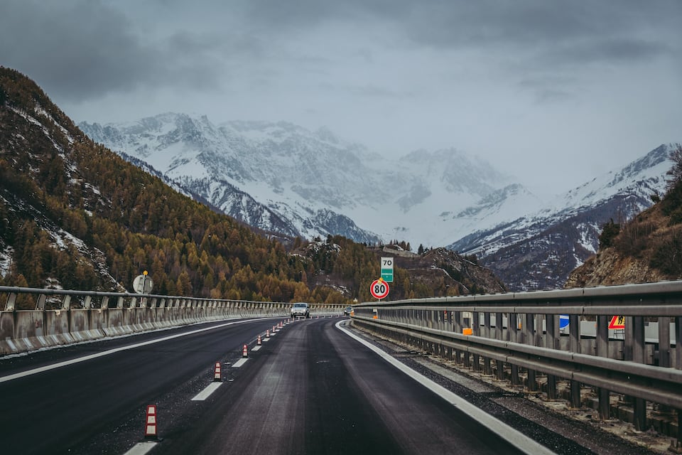Uma autoestrada com sinal de velocidade de 80 km/h, rodeada por montanhas e folhagem outonal.