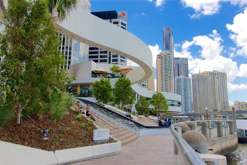 A waterfront promenade with modern architecture, including a curved white structure and high-rise buildings in the background.