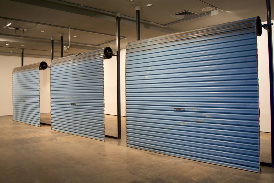 Three closed blue roller doors in a gallery or warehouse.