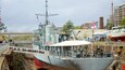 A large ship named A.S. Diamantina docked at a port with industrial structures and buildings in the background.