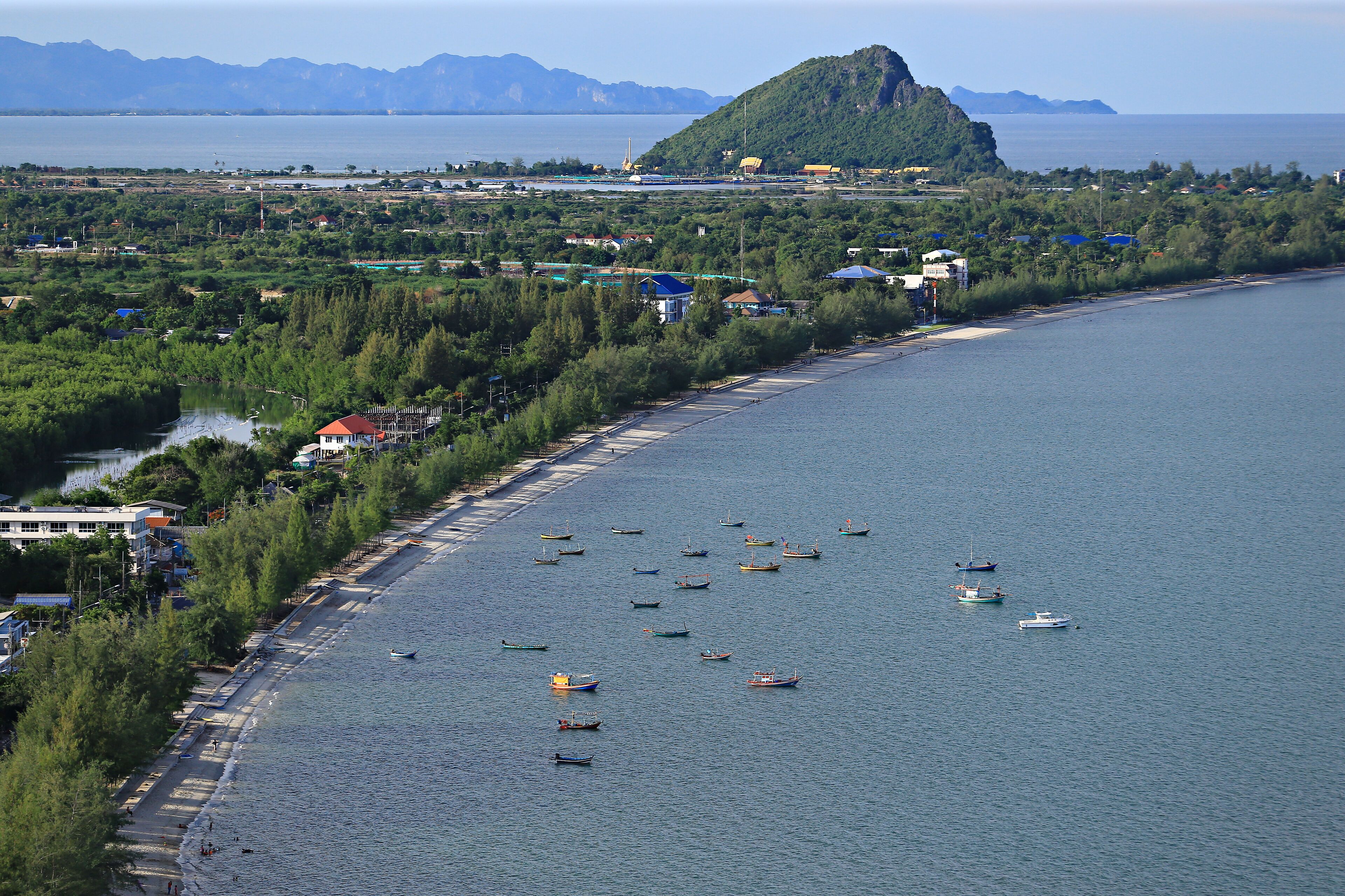 A coastal town with a beach, boats, and a mountain in the background.