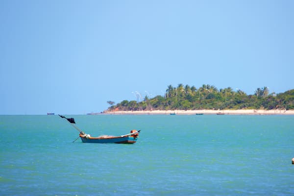 Ein Boot auf ruhigem türkisblauem Wasser mit einem Sandstrand und Palmen im Hintergrund.
