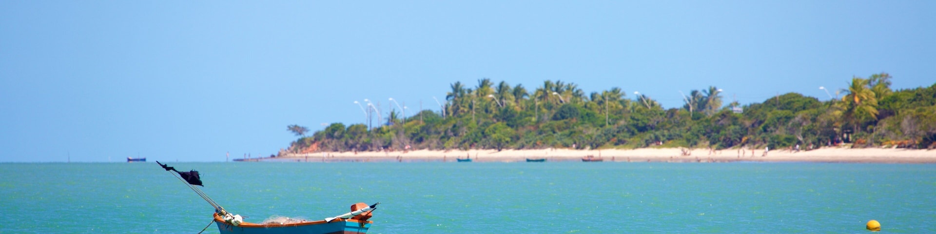 Um barco em águas turquesa calmas, com uma praia de areia e palmeiras ao fundo.