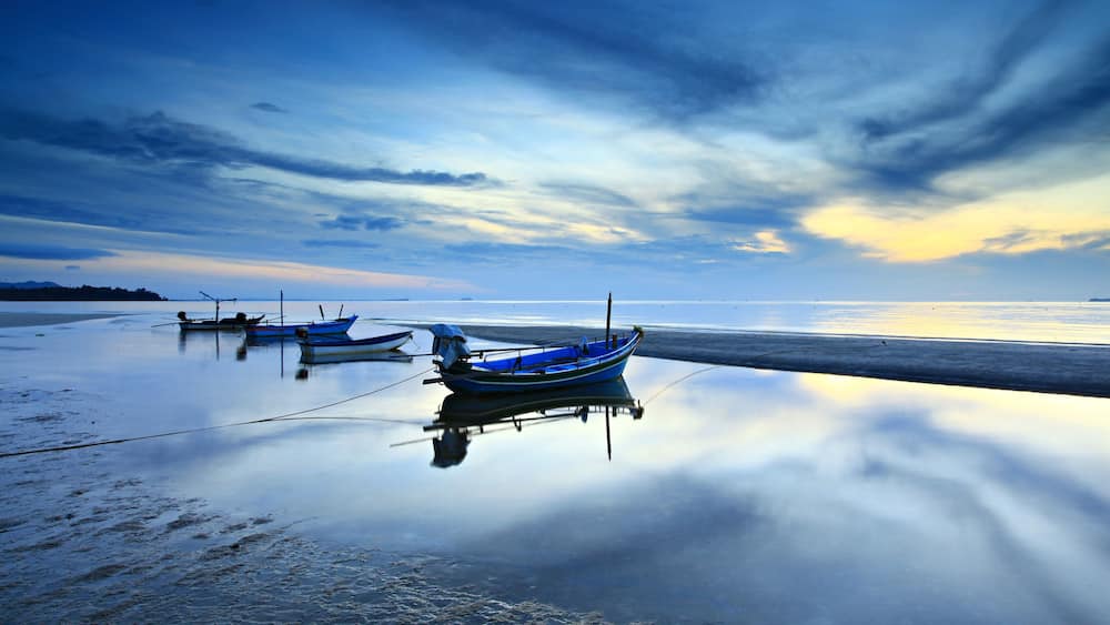 A beach with calm waters and boats anchored near the shore.