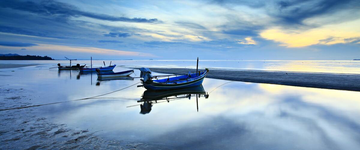 A beach with calm waters and boats anchored near the shore.