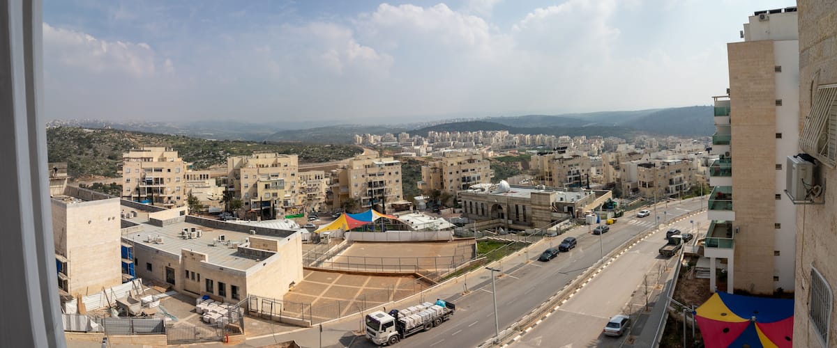 A cityscape with multiple buildings, a road with vehicles, and a distant hilly landscape.
