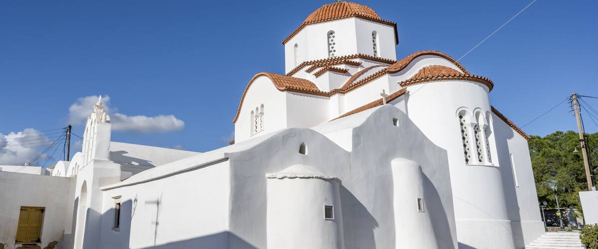 A white church with a red-tiled roof and a stone-paved courtyard.