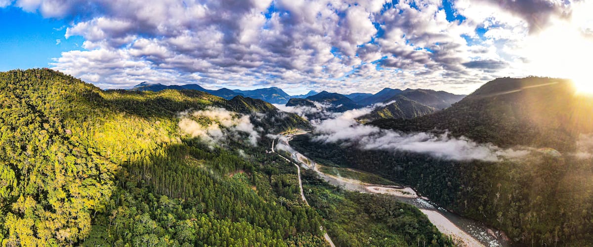 A mountainous landscape with a winding river, dense forest, and a road.