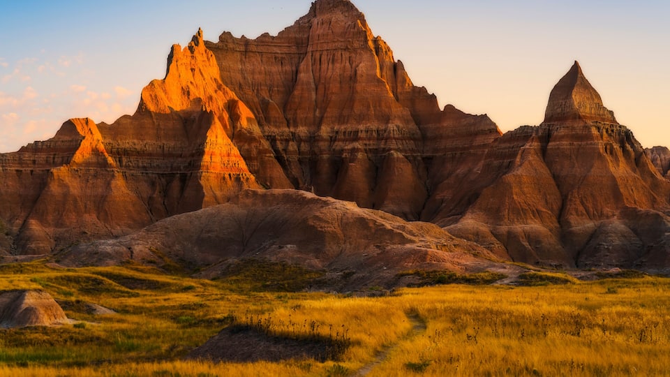 A rugged landscape with prominent buttes and a grassy field.