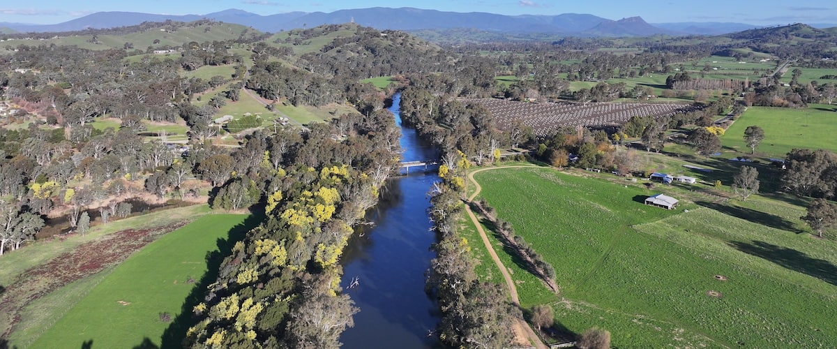 A river winding through a valley with green fields and scattered trees, surrounded by rolling hills and distant mountains.