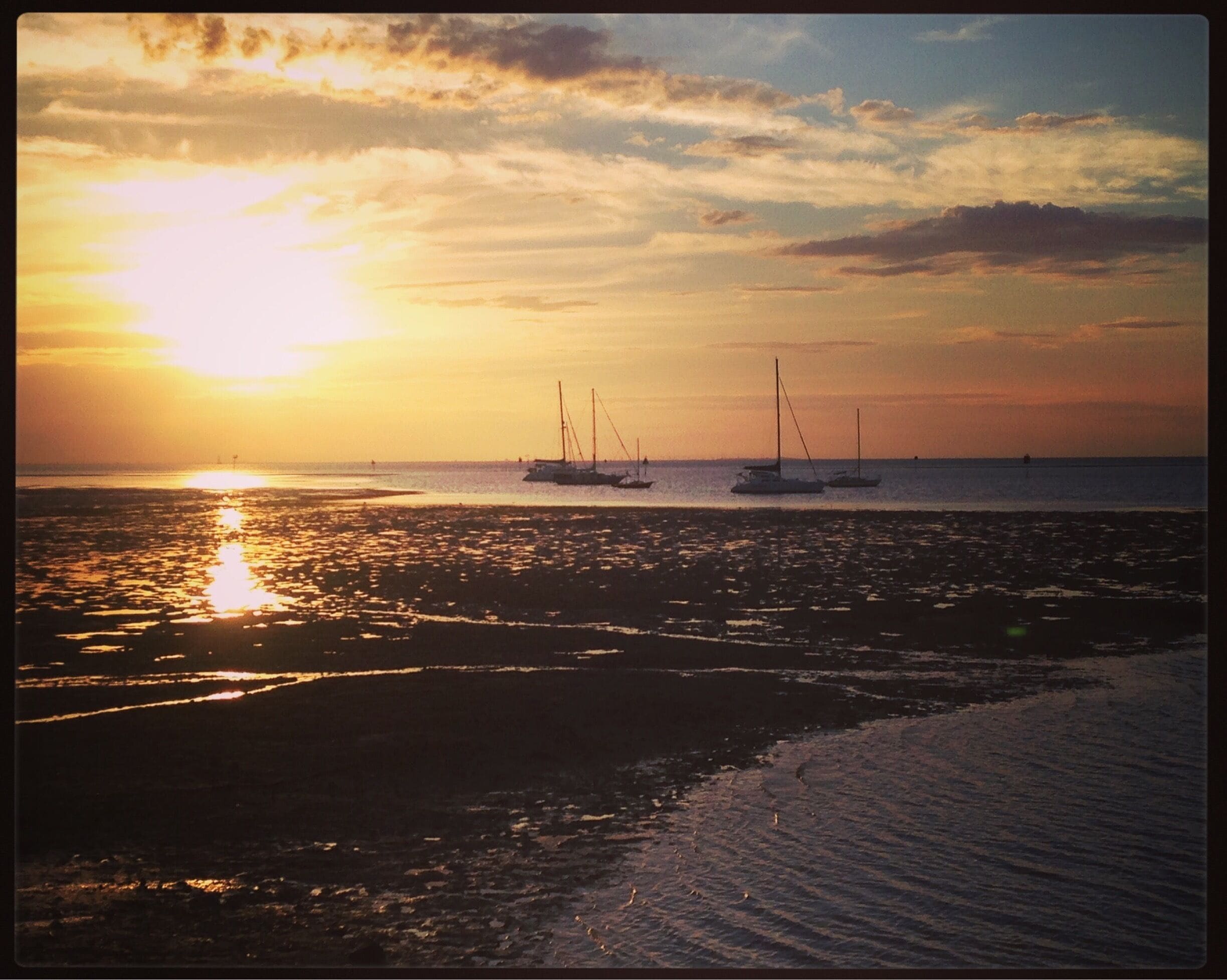 Un atardecer sobre una playa con veleros.