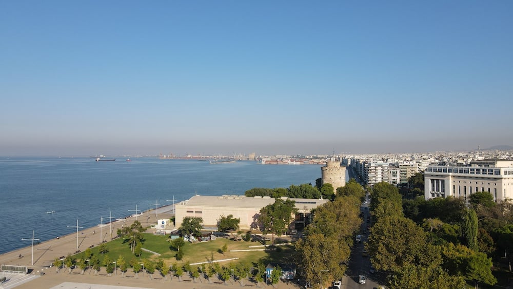 Un paysage urbain côtier avec un château imposant, un port de plaisance et un mélange de bâtiments modernes et historiques.