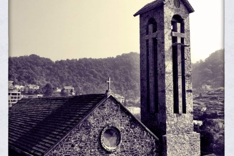 A church with a bell tower and a cross on top, surrounded by a hilly landscape.