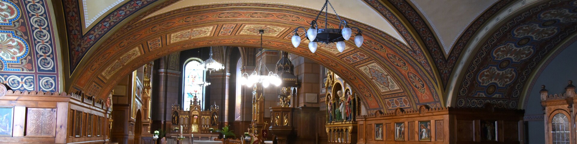 Interior de igreja ornamentado, com altos tetos abobadados, detalhada carpintaria e estátuas religiosas.