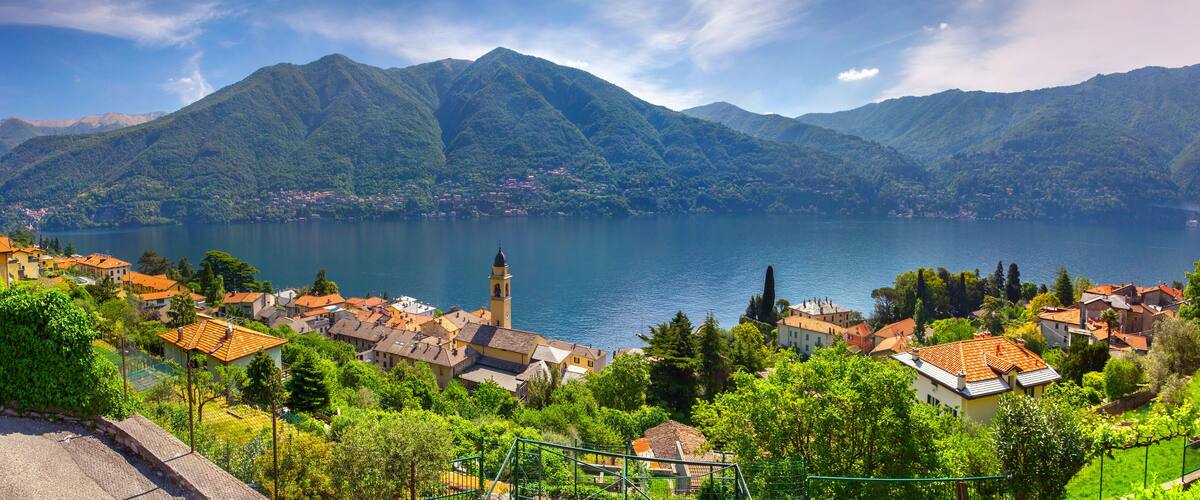 A lake surrounded by mountains, a village with red-roofed houses, and a church with a bell tower.