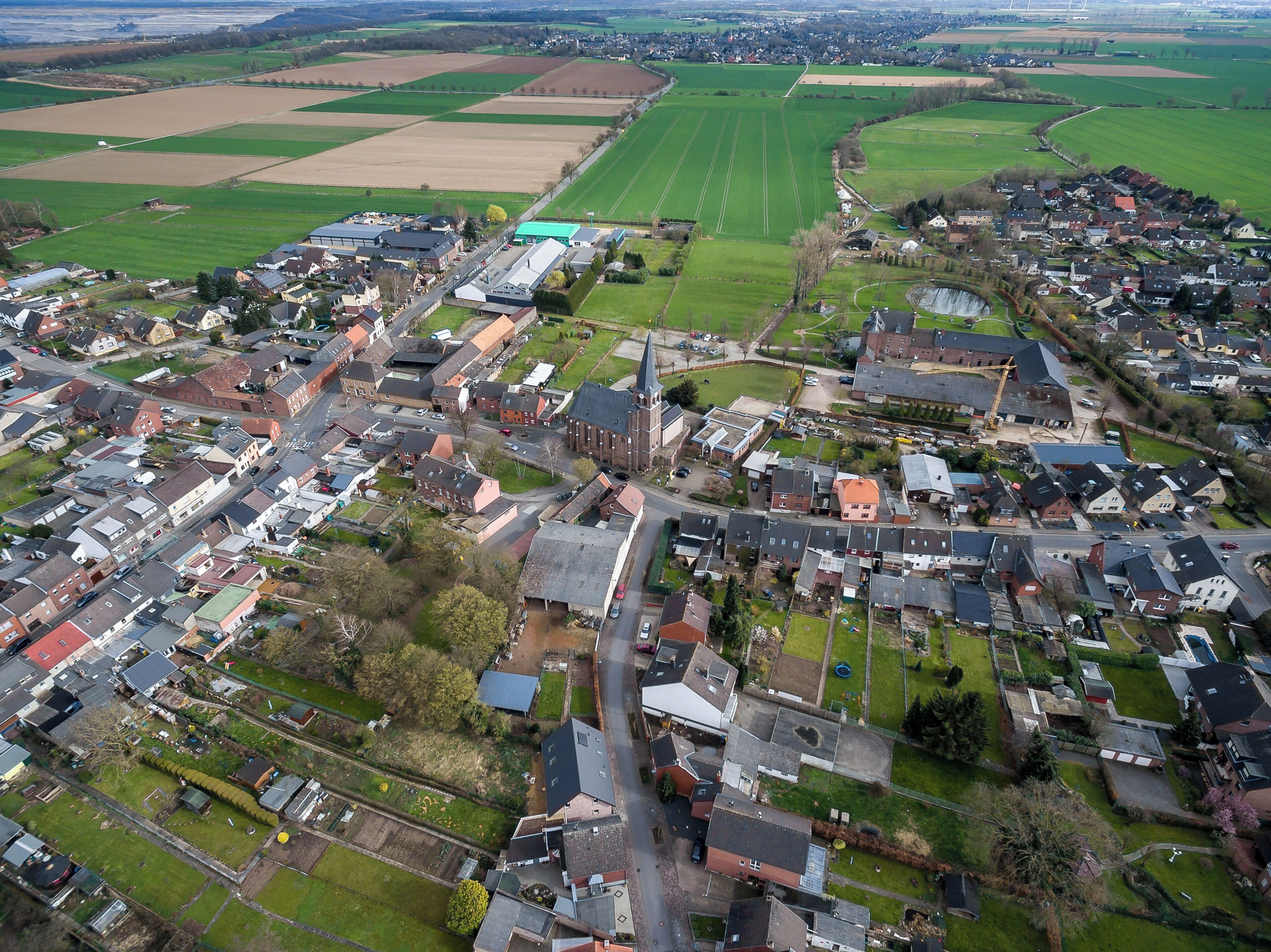 An aerial view of a small town with a mix of residential and commercial buildings, surrounded by green fields and open land.