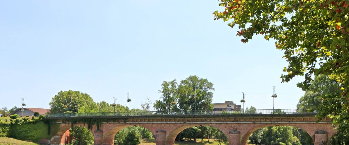 A brick bridge over a river with green grass and trees around.