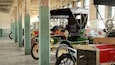 A vintage car exhibition with several antique vehicles displayed under a high ceiling with exposed beams.