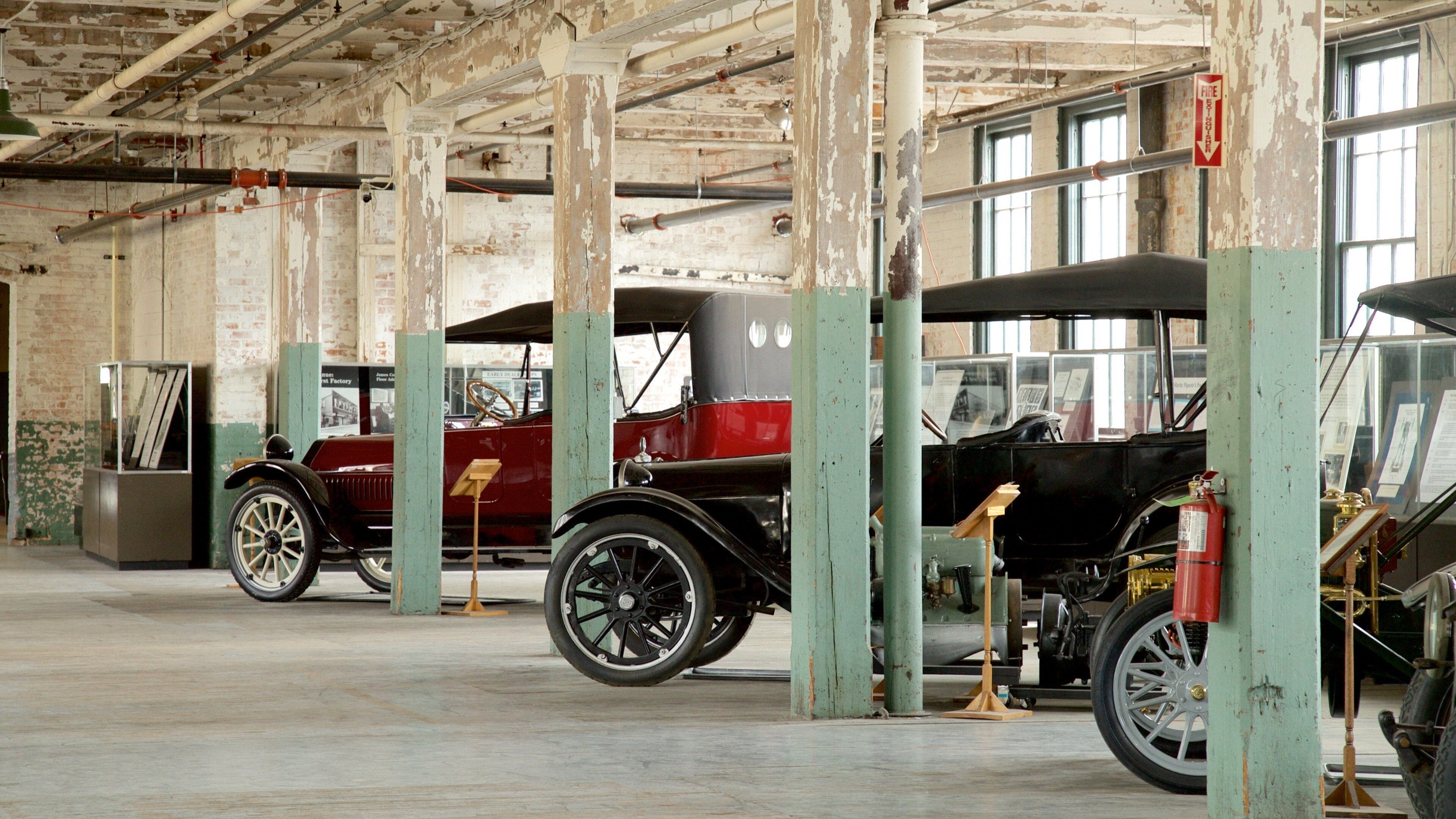 An indoor exhibit with vintage cars, wooden beams, and a fire extinguisher.