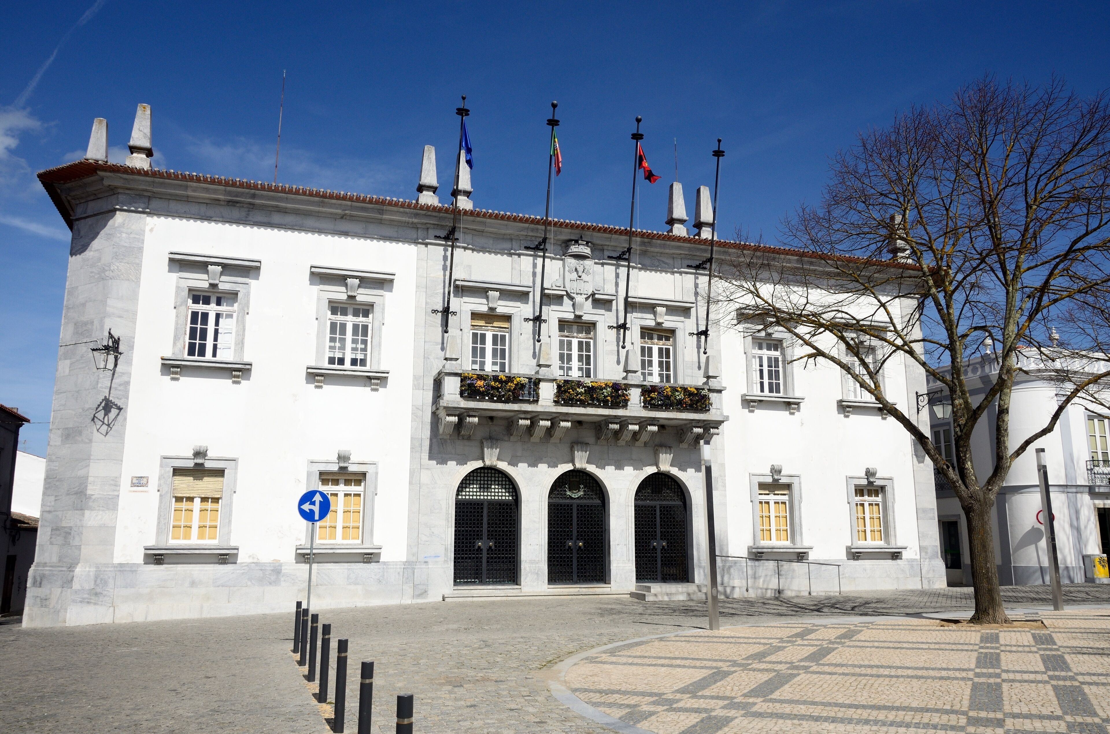 A white building with black doors and windows, a blue sign, and flags.