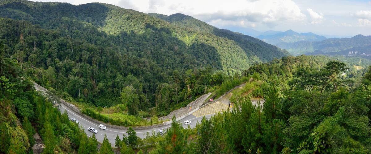 A winding road through a lush, mountainous landscape with dense forests and distant hills.