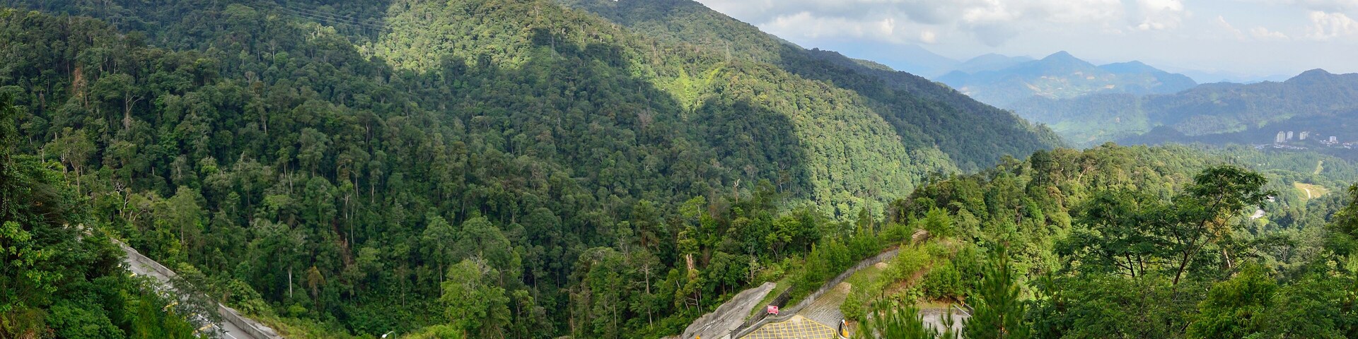 A winding road through a lush, mountainous landscape with dense forests and distant hills.