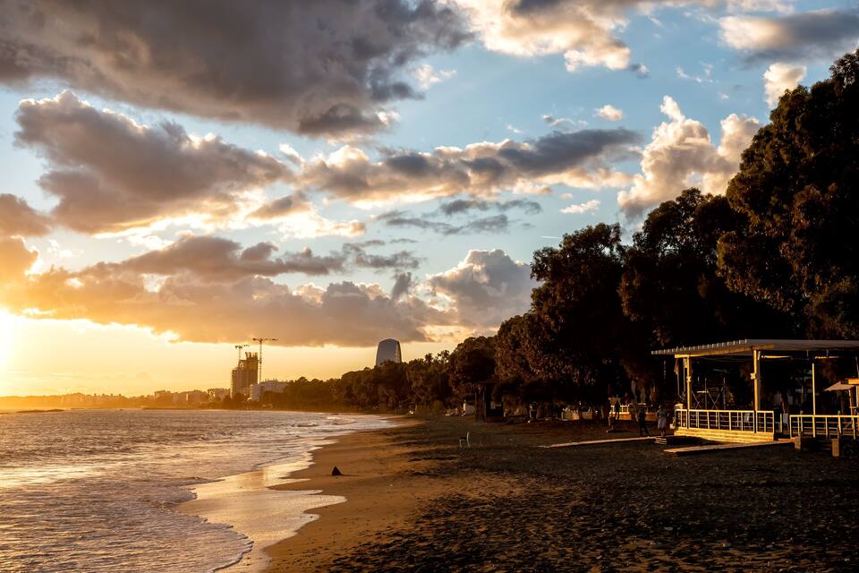 A beach with waves, a pier, and a city skyline in the background.