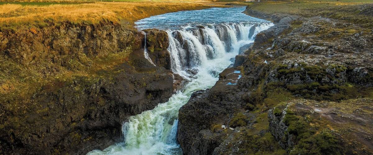 A waterfall cascading down a rocky cliff surrounded by grassy hills.