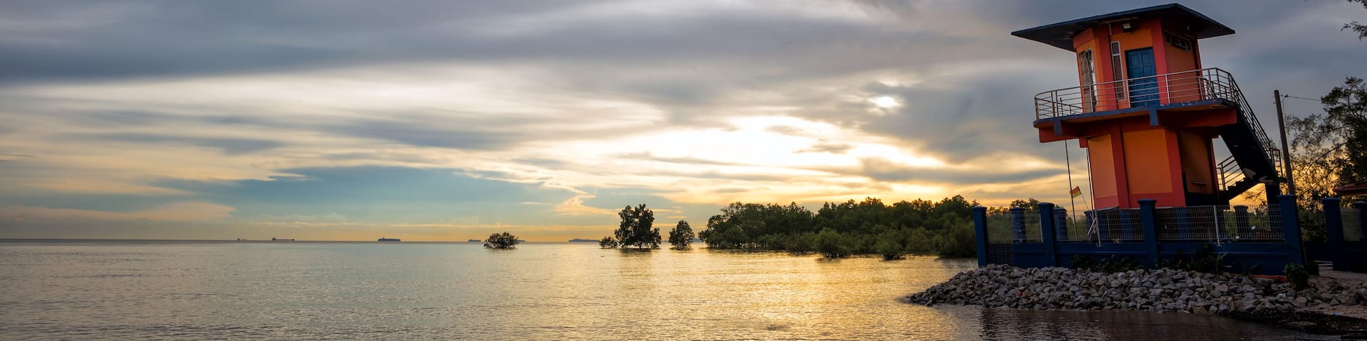 Coastal Guard Tower at Pantai Kelanang, Banting, Malaysia - striking orange coastal guard tower on the edge of Pantai Kelanang beach in Malaysia, overlooking calm waters under a cloudy sky.