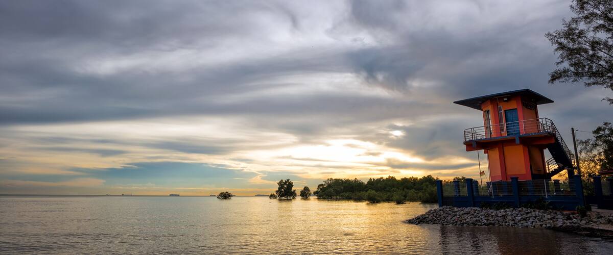 A lighthouse by the water during sunset.