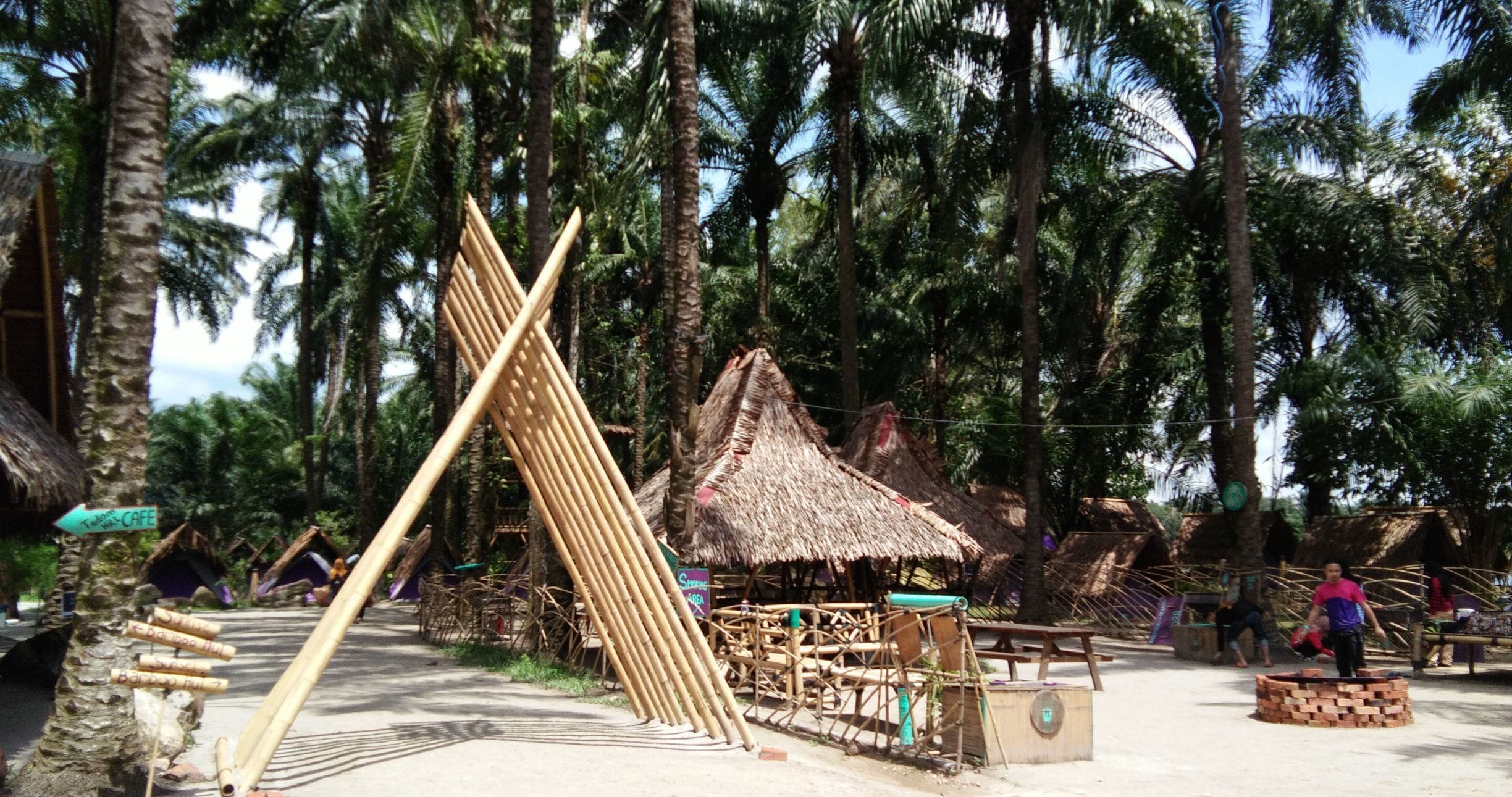A rustic village with bamboo structures, thatched-roof huts, and palm trees.