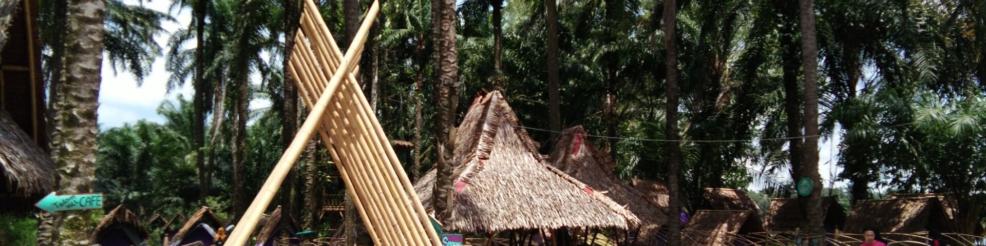 A rustic village with bamboo structures, thatched-roof huts, and palm trees.