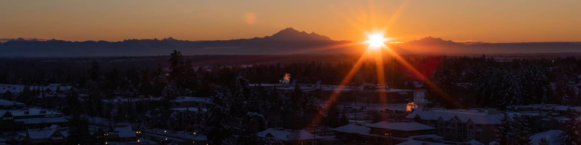 Sunburst over mountains and cityscape at sunset; Surrey, British Columbia, Canada