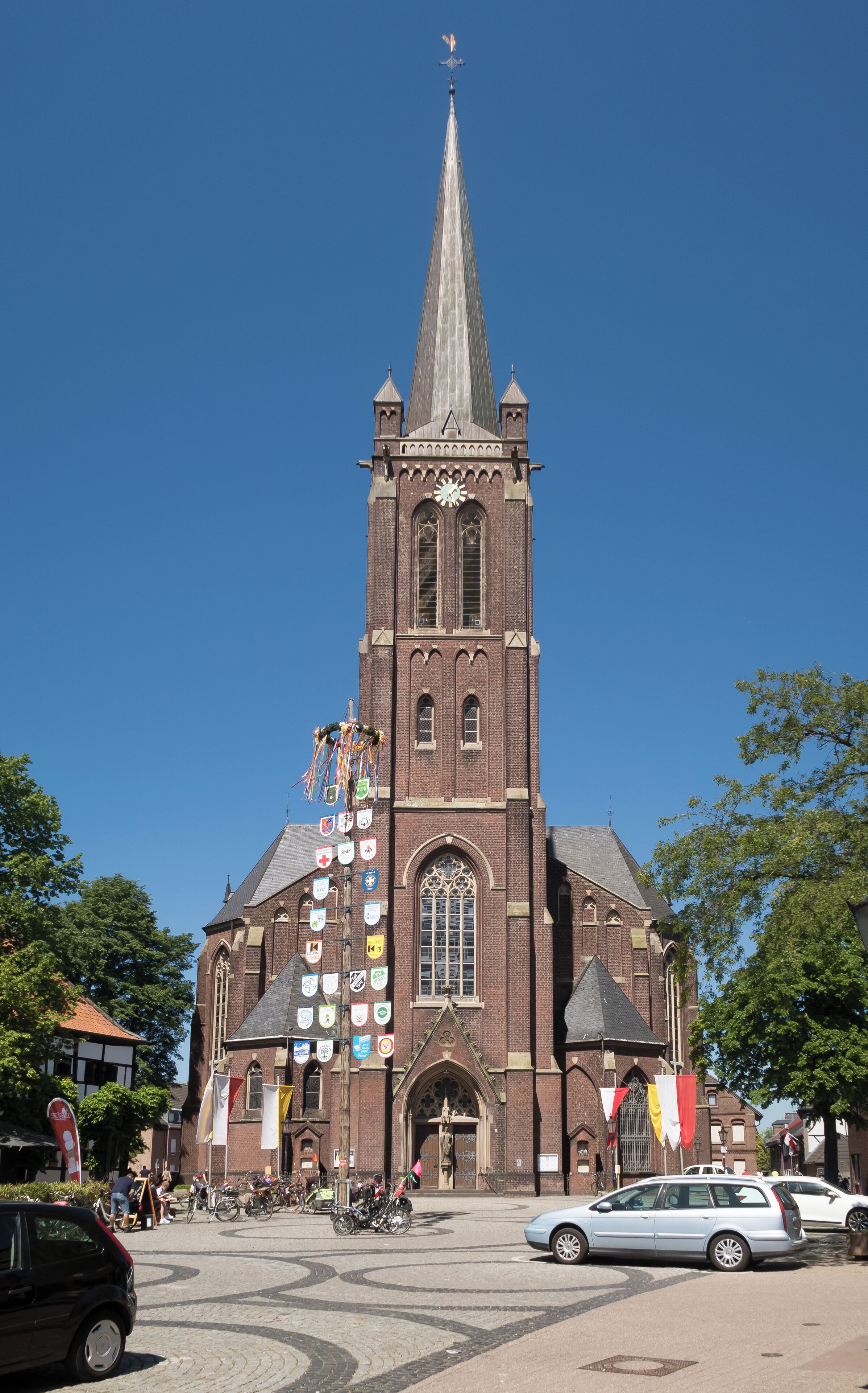 A historic church with a tall spire, a large clock, and multiple flags.