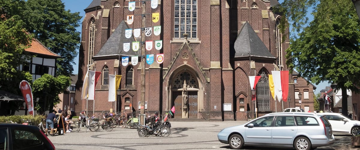 A historic church with a tall spire, a large clock, and multiple flags.