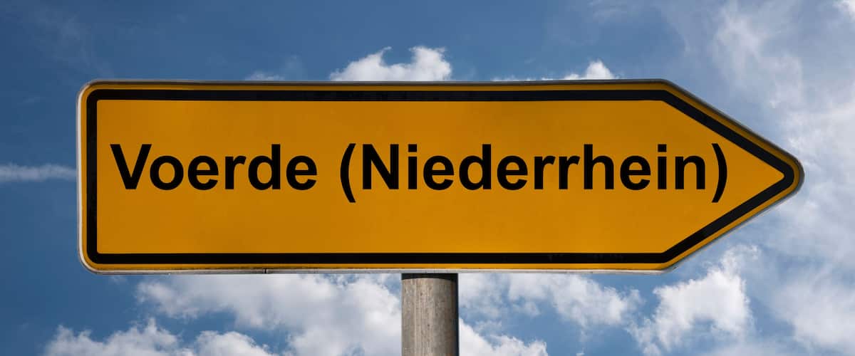 A directional sign with the text "Voerde (Niederrhein)" against a blue sky with clouds.